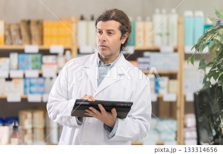Male pharmacist conducting inventory with tablet Male pharmacist conducting inventory with tablet 133314656