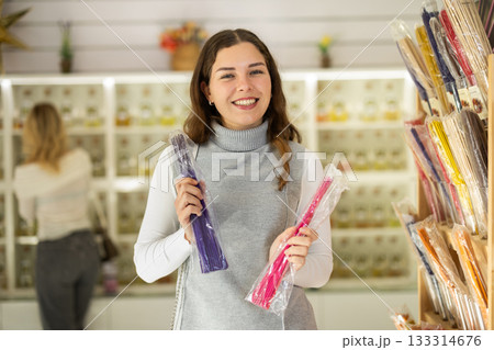 Girl client chooses aroma sticks, inhales fragrance, woman shopping in background Girl client chooses aroma sticks, inhales fragrance, woman shopping in background 133314676
