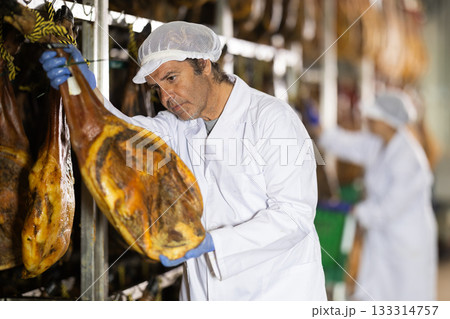 man checks the quality of ham in a factory 133314757