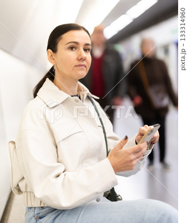 Girl with phone is sitting on metro platform station, scrolling though internet Girl with phone is sitting on metro platform station, scrolling though internet 133314960