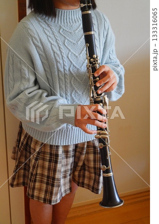 淡いブルーのケーブルニットを着た子どもがクラリネットを構えている縦構図の写真。 133316065