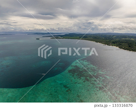 Coastal view with turquoise reef water and green hills under cloudy sky and horizon line. Siargao, Philippines. 133316870