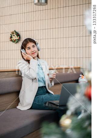 A woman in a cafe listens to music on headphones, holding a coffee cup, with a laptop nearby. Modern and relaxed atmosphere. A woman in a cafe listens to music on headphones, holding a coffee cup, with a laptop nearby. Modern and relaxed atmosphere. 133317268