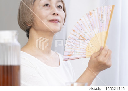 リビングで扇子を扇いで涼むシニア女性 133321543