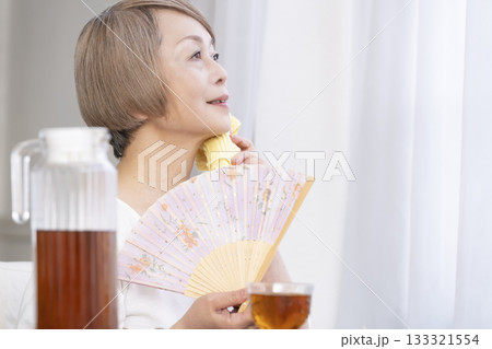 リビングで扇子を扇いで涼むシニア女性 133321554