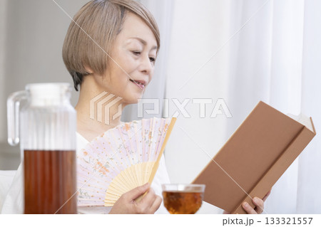 リビングで扇子を扇いで涼むシニア女性 133321557