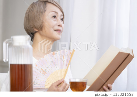リビングで扇子を扇いで涼むシニア女性 133321558