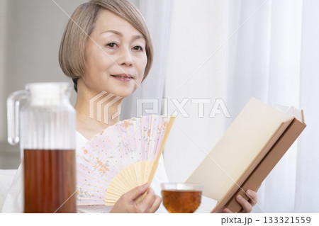 リビングで扇子を扇いで涼むシニア女性 リビングで扇子を扇いで涼むシニア女性 133321559