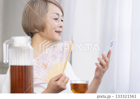 リビングで扇子を扇いで涼むシニア女性 133321561