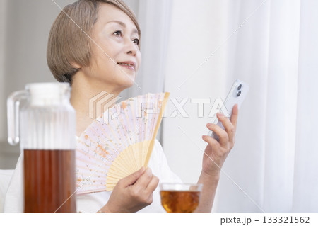 リビングで扇子を扇いで涼むシニア女性 133321562
