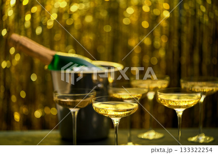 Bottle of champagne in a bucket with ice and glasses on blurred golden stylish background. Space for text. 133322254