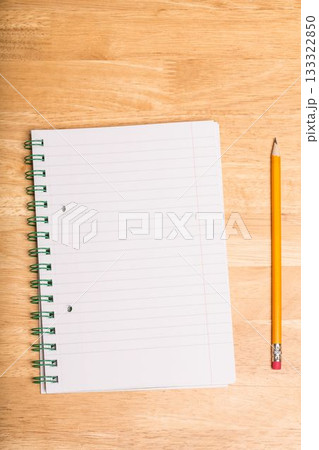 Spiral-bound lined notebook is lying open on wooden tabletop, with yellow pencil resting parallel Spiral-bound lined notebook is lying open on wooden tabletop, with yellow pencil resting parallel 133322850