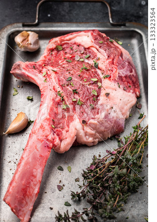 Ready for cooking Tomahawk beef steak with seasonings, raw marbled rib eye with bone on steel tray. black background. top view Ready for cooking Tomahawk beef steak with seasonings, raw marbled rib eye with bone on steel tray. black background. top view 133323564