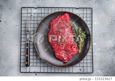 Marinated Skirt machete steak, raw beef meat with thyme and spices on plate. grey background. top view Marinated Skirt machete steak, raw beef meat with thyme and spices on plate. grey background. top view 133323627