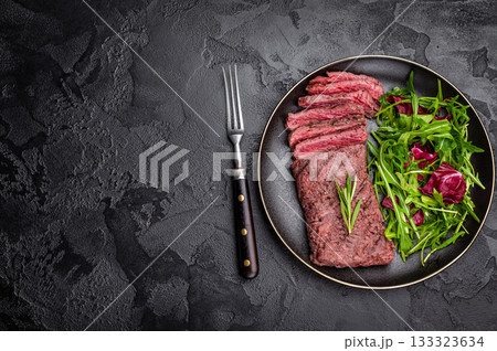Grilled and sliced Flank beef steak on plate with salad. black background. top view Grilled and sliced Flank beef steak on plate with salad. black background. top view 133323634