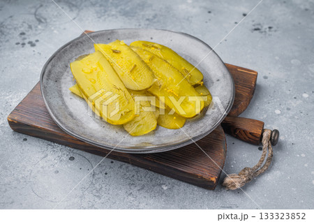 Thin brined pickle slices arranged on a gray plate, crunchy yellow cucumbers with herbs on a cool textured backdrop.. Thin brined pickle slices arranged on a gray plate, crunchy yellow cucumbers with herbs on a cool textured backdrop.. 133323852
