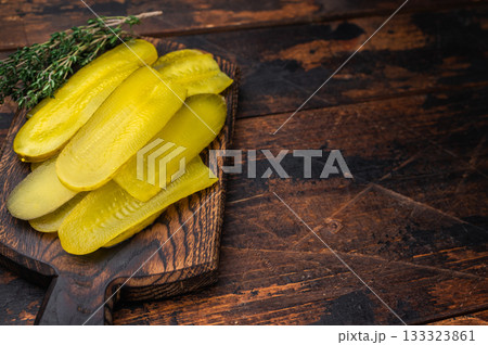 Yellow pickled cucumber slices on rustic wooden cutting board with thyme and peppercorns, top view of brined savory snack. Yellow pickled cucumber slices on rustic wooden cutting board with thyme and peppercorns, top view of brined savory snack. 133323861