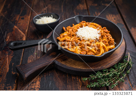 Classic pasta bolognese with savory meat ragu and parmesan shreds served in rustic skillet on vintage wooden surface with herbs. 133323871