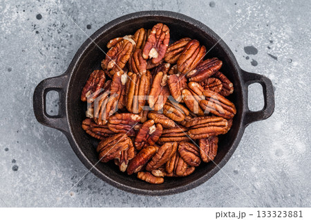 Brown pecan halves displayed in a cast iron pan resting on weathered wood against a grey textured background creating a natural moody food visual 133323881