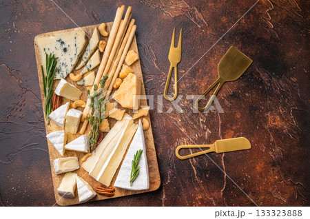 Rustic cheese platter with nuts herbs and breadsticks displayed on a wooden board set against a rich dark textured backdrop. Rustic cheese platter with nuts herbs and breadsticks displayed on a wooden board set against a rich dark textured backdrop. 133323888