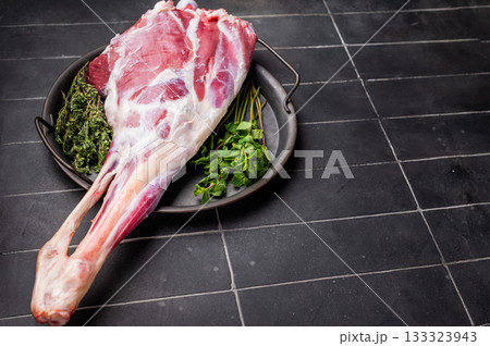 Uncooked whole lamb leg, raw mutton meat with herbs for cooking. black background. top view Uncooked whole lamb leg, raw mutton meat with herbs for cooking. black background. top view 133323943