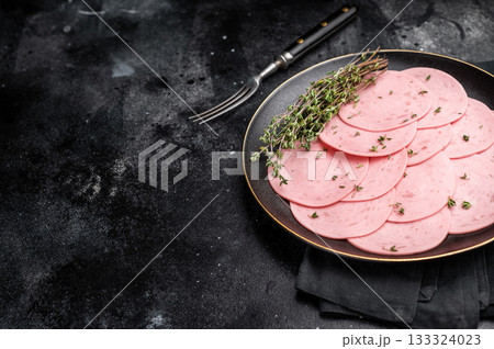 Round slices of pink deli meat (salami/ham) seasoned with thyme, presented on a dark plate for a charcuterie snack or sandwich ingredient. Round slices of pink deli meat (salami/ham) seasoned with thyme, presented on a dark plate for a charcuterie snack or sandwich ingredient. 133324023