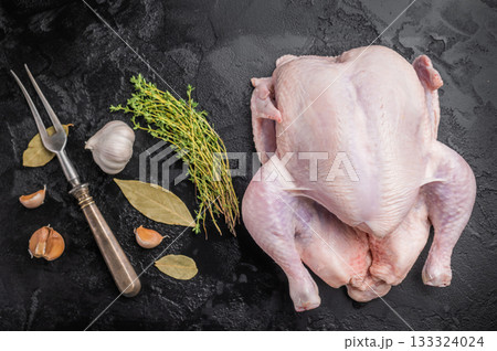 Raw whole chicken with fresh thyme and garlic cloves on a dark, black textured stone background. Preparing to cook poultry. 133324024