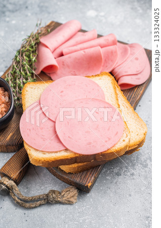 Slices of pink bologna lunch meat on toasted white bread with rock salt and thyme on a wooden board. Grey background with copy space. 133324025