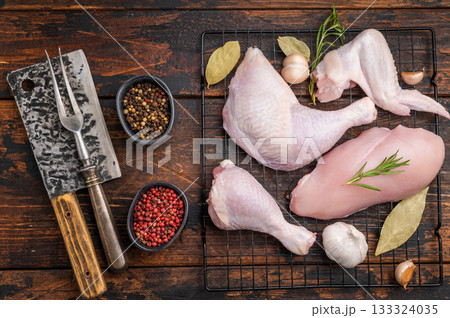 Raw chicken cuts (breast, leg, wing) on a rack with thyme, rosemary, garlic, and peppercorns on dark rustic wood. Ready for seasoning. Raw chicken cuts (breast, leg, wing) on a rack with thyme, rosemary, garlic, and peppercorns on dark rustic wood. Ready for seasoning. 133324035
