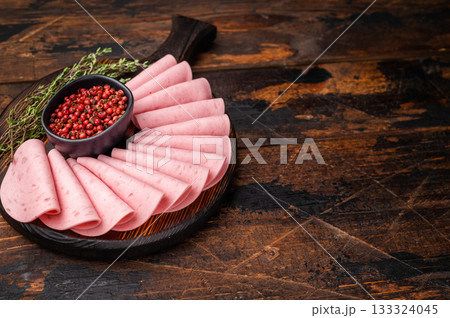 Top view of sliced deli meat (cold cuts) with spices and herbs on a rustic wooden serving board. Copy space. 133324045