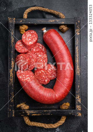 Sliced and whole Turkish sucuk (sujuk) in a rustic tray with a fork. Traditional spicy dry sausage on a dark background. Sliced and whole Turkish sucuk (sujuk) in a rustic tray with a fork. Traditional spicy dry sausage on a dark background. 133324053