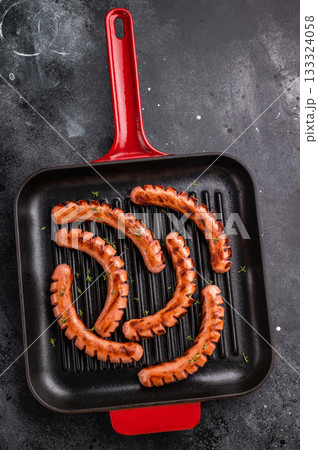 Grilled and cut sausages (wieners/frankfurters) in a hot cast iron grill pan on a dark background. Ready meal concept for dinner or BBQ. 133324058