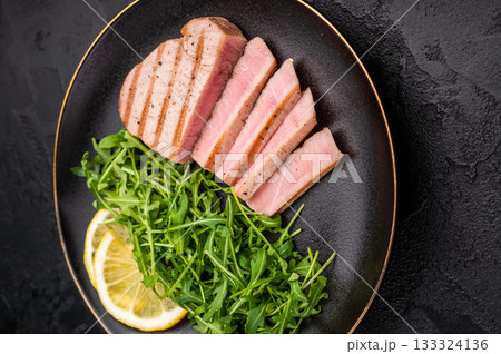 Succulent grilled tuna steak, showcasing vibrant color and rich taste, perfect for summer barbecues and elegant dinners. black background. top view 133324136