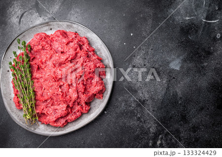 Raw ground wild game meat rabbit hare on a textured grey plate with fresh thyme, set on a dark, moody stone background. 133324429