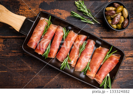 Appetizing plate of thinly sliced cured Italian ham (Prosciutto Crudo) garnished with rosemary sprigs. 133324882