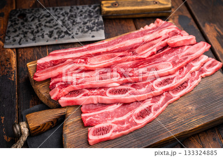 Raw Flanken cut beef short ribs and a rustic cleaver on a dark wooden background with ample copy space. Raw Flanken cut beef short ribs and a rustic cleaver on a dark wooden background with ample copy space. 133324885