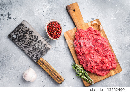 Raw ground venison (wild deer meat) with fresh rosemary and garlic on a wooden board against a modern gray stone background. 133324904
