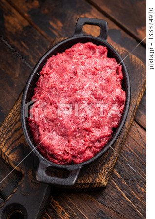 Raw ground wild game meat (venison/boar) in a black skillet on a rustic wooden board, seasoned with fresh thyme and peppercorns. 133324910
