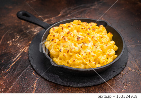 Baked mac and cheese in a black skillet, set against a rustic dark brown background 133324919
