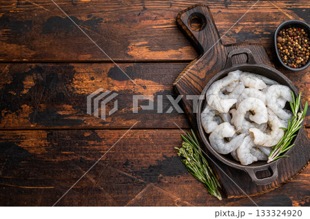 Raw peeled shrimp prawn and rosemary in a dark cast iron skillet on a rustic wooden background. Top view with copy space for recipe or menu. 133324920