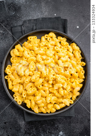 Golden mac and cheese in a black skillet, rustic dark background, fork beside 133324934