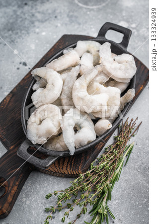 Frozen raw shrimp prawns in a rustic skillet with fresh thyme on a gray stone background. Flat lay with copy space. 133324939
