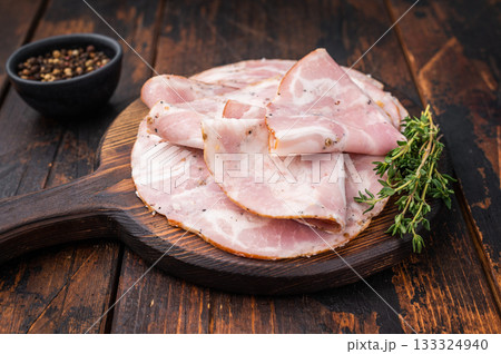 Slices of authentic Italian Pancetta Arrotolata served on a dark rustic cutting board with fresh thyme and peppercorns. 133324940