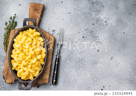 Creamy mac and cheese in a black cast iron skillet, resting on a rustic wooden board against a gray background. 133324945