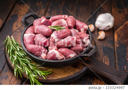 Raw chicken hearts in cast iron skillet, surrounded by garlic and rosemary on rustic wooden background 133324997
