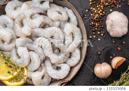 Raw peeled shrimp prawn with lemon and thyme in a metal pan on a textured black background. Maximum contrast with copy space. Raw peeled shrimp prawn with lemon and thyme in a metal pan on a textured black background. Maximum contrast with copy space. 133325006