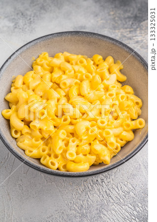 Creamy macaroni and cheese in a rustic bowl on a wooden board, set against a textured gray background 133325031