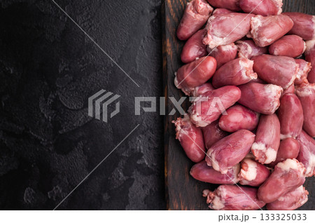 Raw chicken hearts with rosemary on dark wooden board and black stone background, fresh poultry offal ready for cooking. 133325033