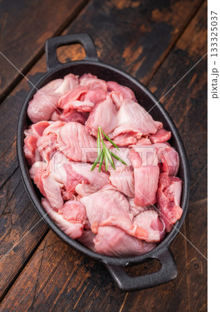 Uncooked gizzards displayed in a dark pan with fresh rosemary and garlic cloves, warm wooden backdrop enhances the rustic feel 133325037