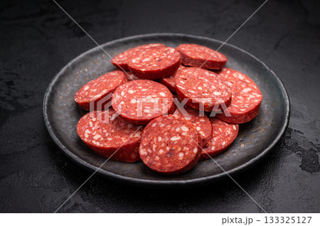 Pile of sliced Turkish sucuk (sujuk) on a dark plate. Traditional spicy dry-cured sausage, ready to eat. 133325127